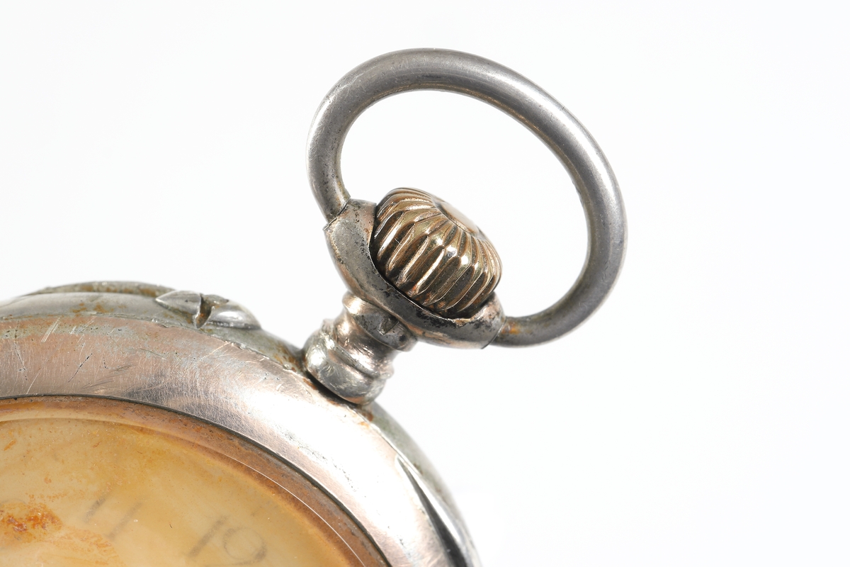 Fickur i silver som dras upp med krona. Runt kronan finns en bygel för att fästa en klockkedja. Den främre boetten har ett glas monterat framför urtavlan som består av vit emalj. Visarna är utsirade i guldfärg, och nedtill en mindre urtavla för sekundvisning. Bakboetten har ett mönstrat motiv liknande det svenska riksvapnet med två lejon på vardera sidan om en sköld krönt med en krona. Boettens ytterkanter är guldförgyllda. Ytterboettens insida har en stämpel liknande en halvmåne och en kungakrona, samt en större och en mindre som liknar en orre. Vidare finns numret "304070" och "0.800" inramat. Även "GALONNE" finns stämplat och siffran "11". Innerboettens utsida har ett graverat mönster bestående av ett liggande lejon med en sköld med de tre svenska kronorna vid sidan om. Vidare finns texten "1/2 CHRONOMETRE REMONTOIR SPIRAL BREGUET" och "CHATON OR 19 RUBIS" samt "BALANCIER COMPENSSÉ". Innerboettens insida har numret "304070" och stämpeln liknande halvmåne och krona inslaget, samt "0.800" inramat. Verket utan stämplar. 
Klockans skyddsboett i två delar, består av en överdel med ett fönster i celluloid, och en underdel att lägga uret i. Baksidan märkt med "23 1/2" och "Herkules D.R.G.M. 160717". Dosan troligen i nickel.