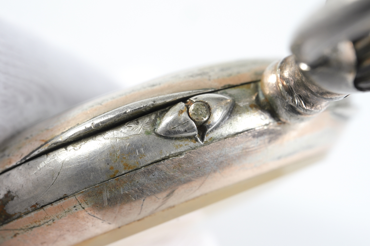 Fickur i silver som dras upp med krona. Runt kronan finns en bygel för att fästa en klockkedja. Den främre boetten har ett glas monterat framför urtavlan som består av vit emalj. Visarna är utsirade i guldfärg, och nedtill en mindre urtavla för sekundvisning. Bakboetten har ett mönstrat motiv liknande det svenska riksvapnet med två lejon på vardera sidan om en sköld krönt med en krona. Boettens ytterkanter är guldförgyllda. Ytterboettens insida har en stämpel liknande en halvmåne och en kungakrona, samt en större och en mindre som liknar en orre. Vidare finns numret "304070" och "0.800" inramat. Även "GALONNE" finns stämplat och siffran "11". Innerboettens utsida har ett graverat mönster bestående av ett liggande lejon med en sköld med de tre svenska kronorna vid sidan om. Vidare finns texten "1/2 CHRONOMETRE REMONTOIR SPIRAL BREGUET" och "CHATON OR 19 RUBIS" samt "BALANCIER COMPENSSÉ". Innerboettens insida har numret "304070" och stämpeln liknande halvmåne och krona inslaget, samt "0.800" inramat. Verket utan stämplar. 
Klockans skyddsboett i två delar, består av en överdel med ett fönster i celluloid, och en underdel att lägga uret i. Baksidan märkt med "23 1/2" och "Herkules D.R.G.M. 160717". Dosan troligen i nickel.