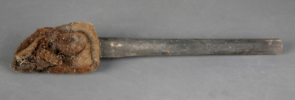 En kort trestokk med en festet ullfille på enden, trolig en gammel ullvott