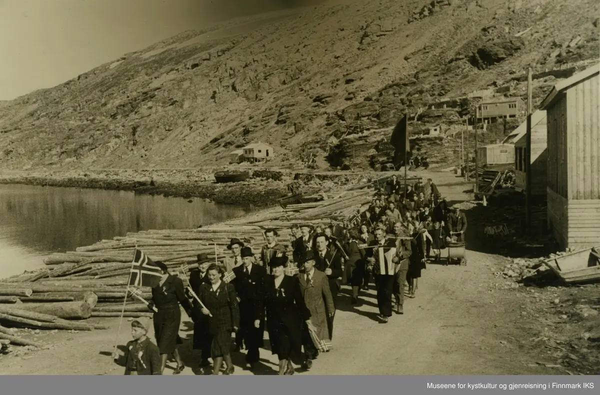 17. mai toget i Hammerfest går langs Nedre Molla i 1946. Toget ledes av en gutt med et større Norges flagg. Bak ham går det finkledde personer med mindre flagg. Man kan se en mann med trekkspill, barn, barnevogner samt et kjøretøy eller vogn og en sykkel bakerst i toget. Lenger bak bæres det en stor flagg, muligens byens isbjørnflagg. 
I Mollafjæra ligger det en stor mengde tømmerstokker samt båter og en pramme. Til høyre i bilde ser man brakker og stolper som enda er uten strømledninger.