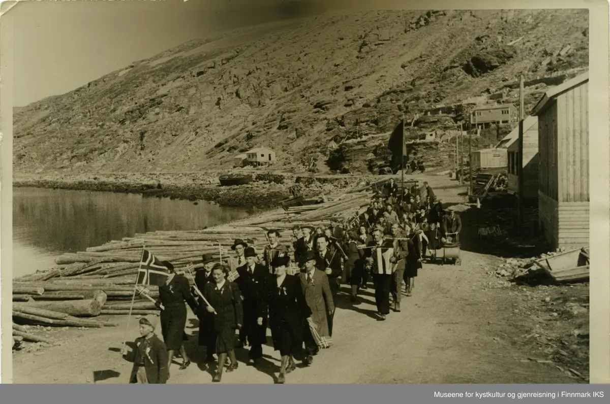 17. mai toget i Hammerfest går langs Nedre Molla i 1946. Toget ledes av en gutt med et større Norges flagg. Bak ham går det finkledde personer med mindre flagg. Man kan se en mann med trekkspill, barn, barnevogner samt et kjøretøy eller vogn og en sykkel bakerst i toget. Lenger bak bæres det en stor flagg, muligens byens isbjørnflagg. 
I Mollafjæra ligger det en stor mengde tømmerstokker samt båter og en pramme. Til høyre i bilde ser man brakker og stolper som enda er uten strømledninger.