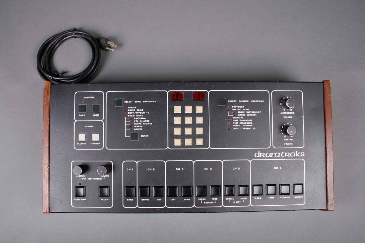 Elektronisk trommemaskin. Panel i kasse med kanter av treverk. Ledning og utganger på baksiden. Toppen av kassen er panel for innstillinger av trommelydene. Seks kanaler kan velges. Mange ulike funksjoner for opptak.