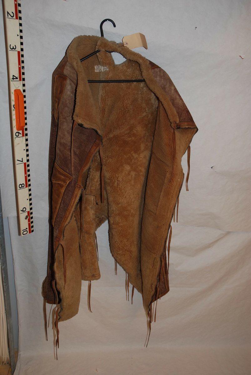 Jakken er brun, godt foret innvendig. Utsiden er av skinn og det er skinn/lær remmer for å stenge jakken. 