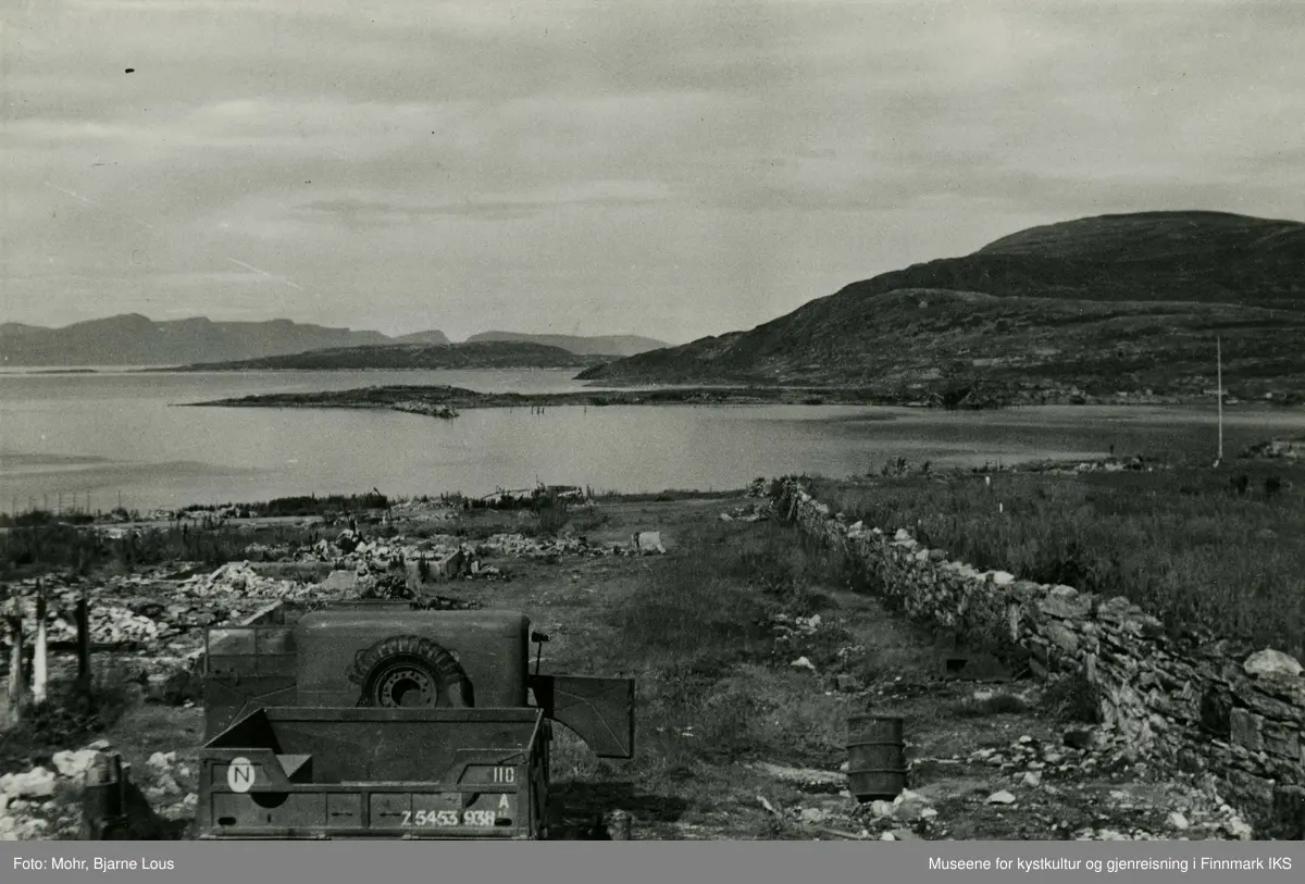 Ødeleggelsene på Hauen i Hammerfest sentrum etter andre verdenskrig. Kirkegårdsmuren står til høyre. Det er parkert en lastebil til venstre. I bakgrunn ser man Fuglenes og Melkøya.