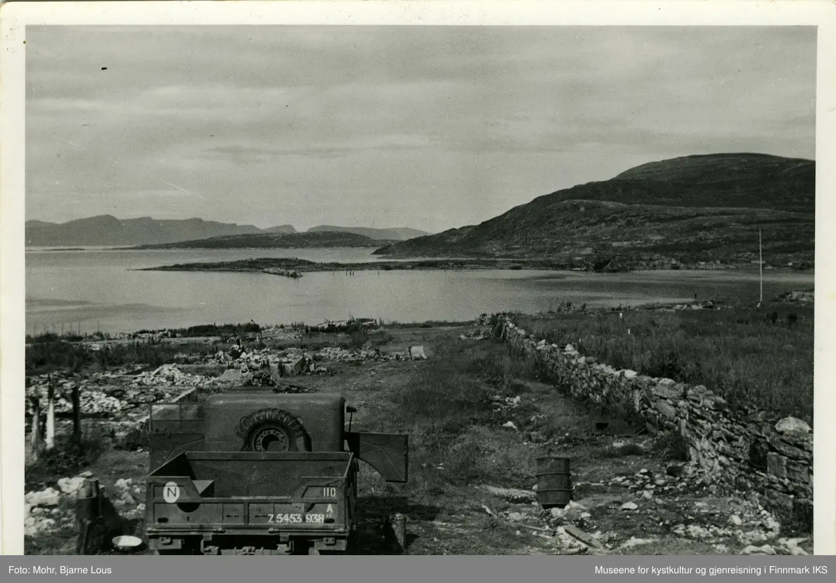 Ødeleggelsene på Hauen i Hammerfest sentrum etter andre verdenskrig. Kirkegårdsmuren står til høyre. Det er parkert en lastebil til venstre. I bakgrunn ser man Fuglenes og Melkøya.