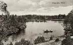 Helgasjön, Växjö, ca 1912. Några personer är ute och ror i en eka. I bakgrunden skymtar några villor bland buskagen.