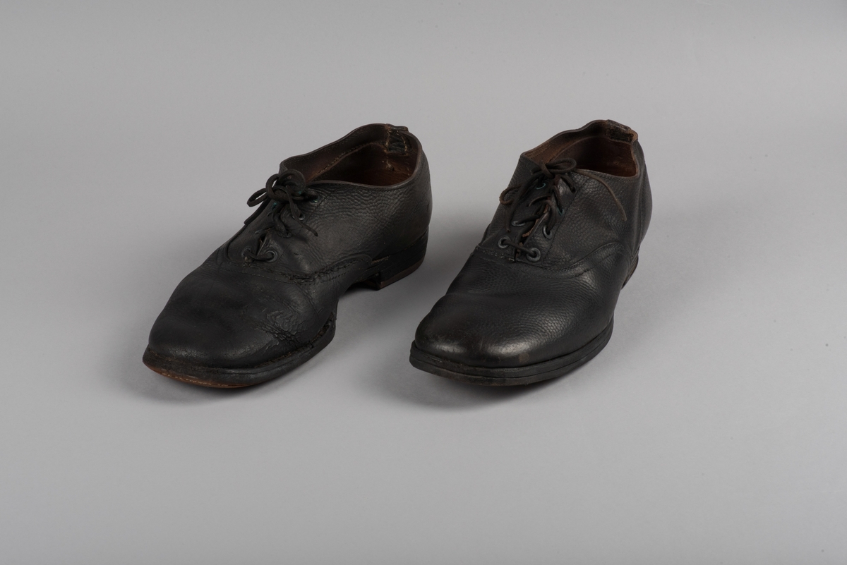 Herrsko, ett par, av skinn (läder) med sula av läder. Klacken skodd med metallsko i U-form. fyra par hål med öljetter i metall och lädersnöre. Ofodrade. Möjligen storlek 46 eller 40. Skinnet är präglat med ett möster av små stjärnor. 

På den högra skon är metallskoningen på klacken vänd, troligen omspikad. 

Skorna hör till en uppsättning kläder för en manlig fånge. 
Kläderna består av en kort dubbelknäppt rock, ett par byxor, en väst av grå vadmal, en mössa och en skjorta av oblekt linne.