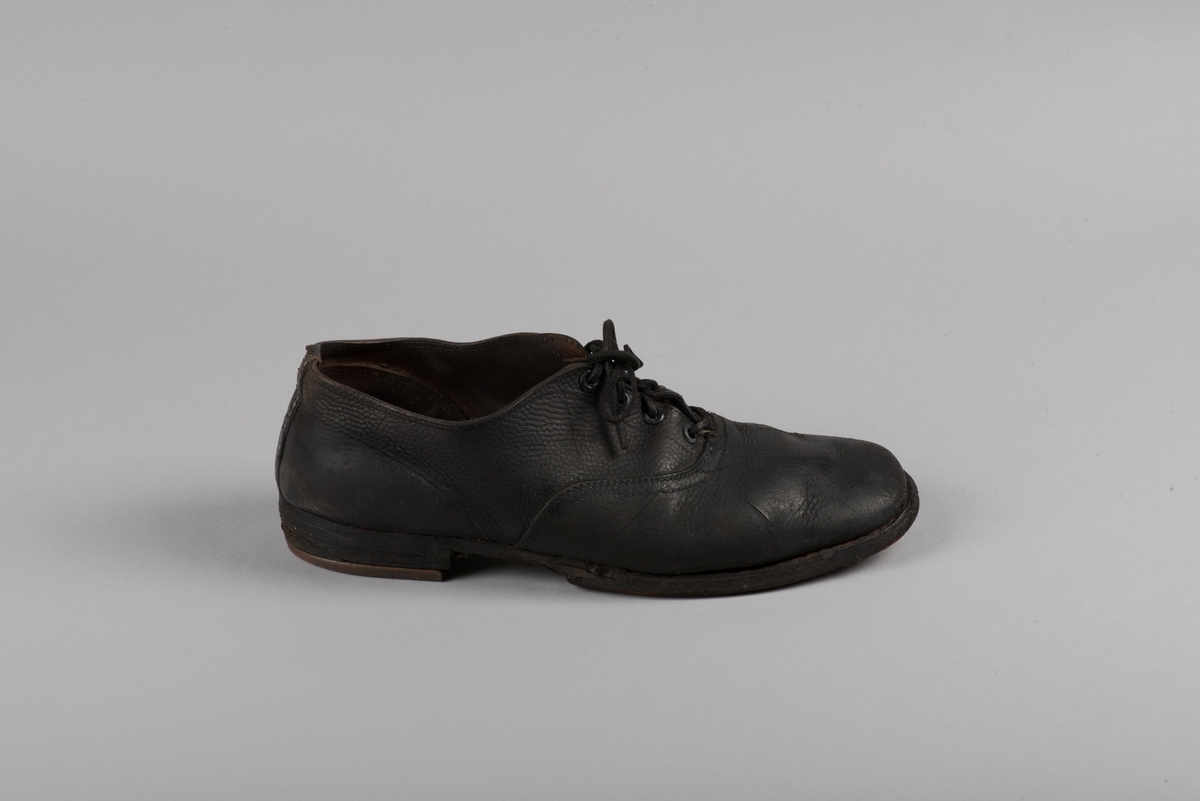 Herrsko, ett par, av skinn (läder) med sula av läder. Klacken skodd med metallsko i U-form. fyra par hål med öljetter i metall och lädersnöre. Ofodrade. Möjligen storlek 46 eller 40. Skinnet är präglat med ett möster av små stjärnor. 

På den högra skon är metallskoningen på klacken vänd, troligen omspikad. 

Skorna hör till en uppsättning kläder för en manlig fånge. 
Kläderna består av en kort dubbelknäppt rock, ett par byxor, en väst av grå vadmal, en mössa och en skjorta av oblekt linne.