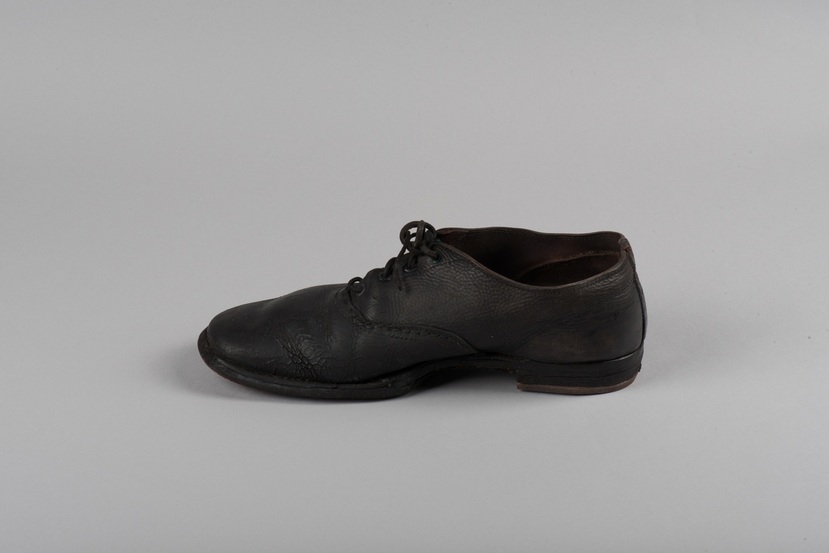 Herrsko, ett par, av skinn (läder) med sula av läder. Klacken skodd med metallsko i U-form. fyra par hål med öljetter i metall och lädersnöre. Ofodrade. Möjligen storlek 46 eller 40. Skinnet är präglat med ett möster av små stjärnor. 

På den högra skon är metallskoningen på klacken vänd, troligen omspikad. 

Skorna hör till en uppsättning kläder för en manlig fånge. 
Kläderna består av en kort dubbelknäppt rock, ett par byxor, en väst av grå vadmal, en mössa och en skjorta av oblekt linne.