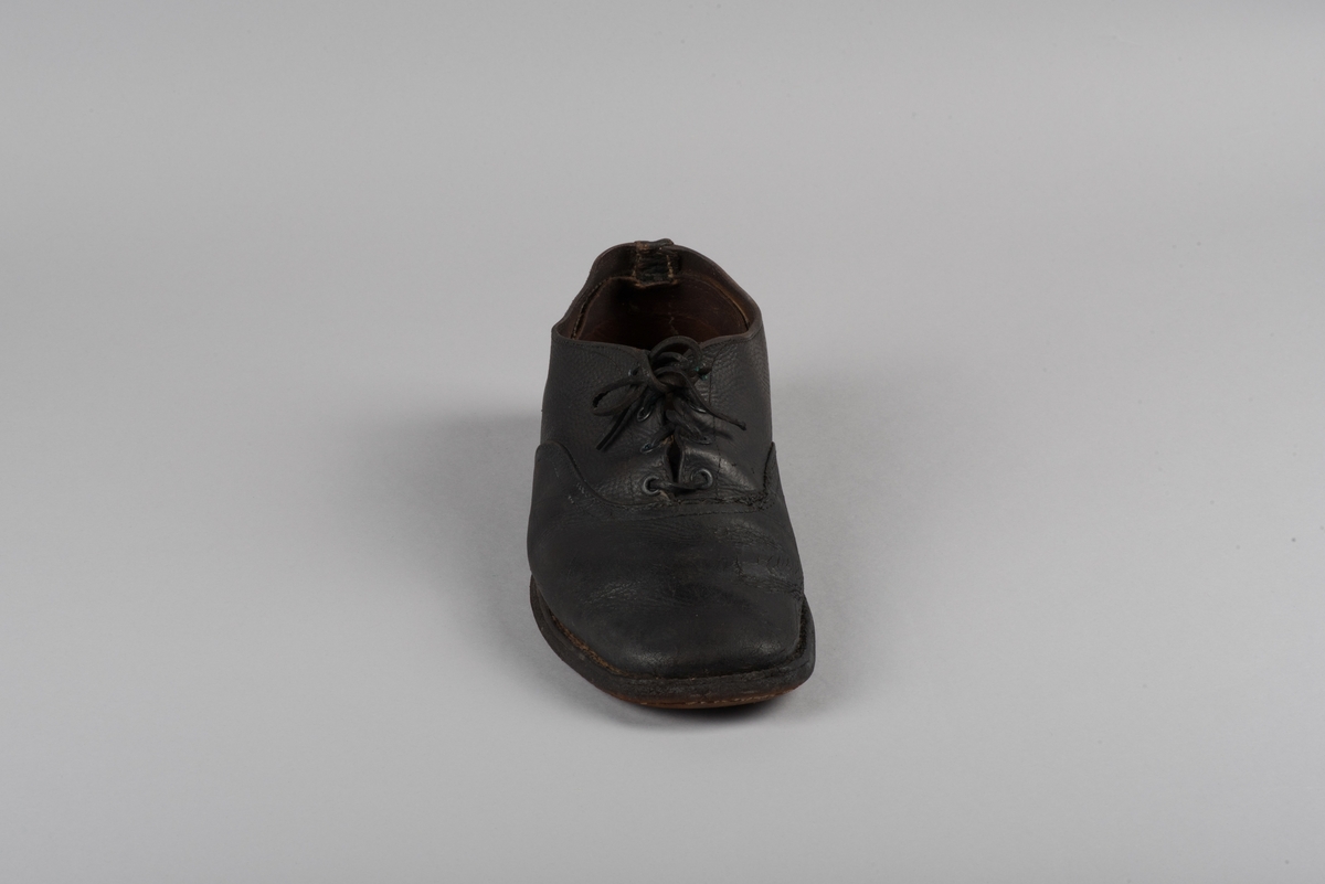 Herrsko, ett par, av skinn (läder) med sula av läder. Klacken skodd med metallsko i U-form. fyra par hål med öljetter i metall och lädersnöre. Ofodrade. Möjligen storlek 46 eller 40. Skinnet är präglat med ett möster av små stjärnor. 

På den högra skon är metallskoningen på klacken vänd, troligen omspikad. 

Skorna hör till en uppsättning kläder för en manlig fånge. 
Kläderna består av en kort dubbelknäppt rock, ett par byxor, en väst av grå vadmal, en mössa och en skjorta av oblekt linne.