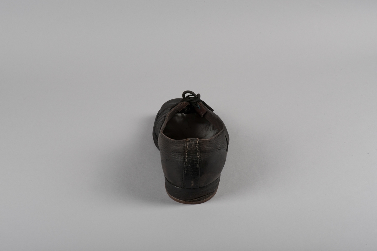 Herrsko, ett par, av skinn (läder) med sula av läder. Klacken skodd med metallsko i U-form. fyra par hål med öljetter i metall och lädersnöre. Ofodrade. Möjligen storlek 46 eller 40. Skinnet är präglat med ett möster av små stjärnor. 

På den högra skon är metallskoningen på klacken vänd, troligen omspikad. 

Skorna hör till en uppsättning kläder för en manlig fånge. 
Kläderna består av en kort dubbelknäppt rock, ett par byxor, en väst av grå vadmal, en mössa och en skjorta av oblekt linne.