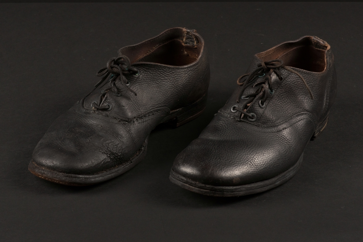 Herrsko, ett par, av skinn (läder) med sula av läder. Klacken skodd med metallsko i U-form. fyra par hål med öljetter i metall och lädersnöre. Ofodrade. Möjligen storlek 46 eller 40. Skinnet är präglat med ett möster av små stjärnor. 

På den högra skon är metallskoningen på klacken vänd, troligen omspikad. 

Skorna hör till en uppsättning kläder för en manlig fånge. 
Kläderna består av en kort dubbelknäppt rock, ett par byxor, en väst av grå vadmal, en mössa och en skjorta av oblekt linne.