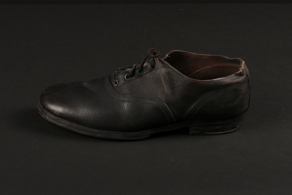 Herrsko, ett par, av skinn (läder) med sula av läder. Klacken skodd med metallsko i U-form. fyra par hål med öljetter i metall och lädersnöre. Ofodrade. Möjligen storlek 46 eller 40. Skinnet är präglat med ett möster av små stjärnor. 

På den högra skon är metallskoningen på klacken vänd, troligen omspikad. 

Skorna hör till en uppsättning kläder för en manlig fånge. 
Kläderna består av en kort dubbelknäppt rock, ett par byxor, en väst av grå vadmal, en mössa och en skjorta av oblekt linne.