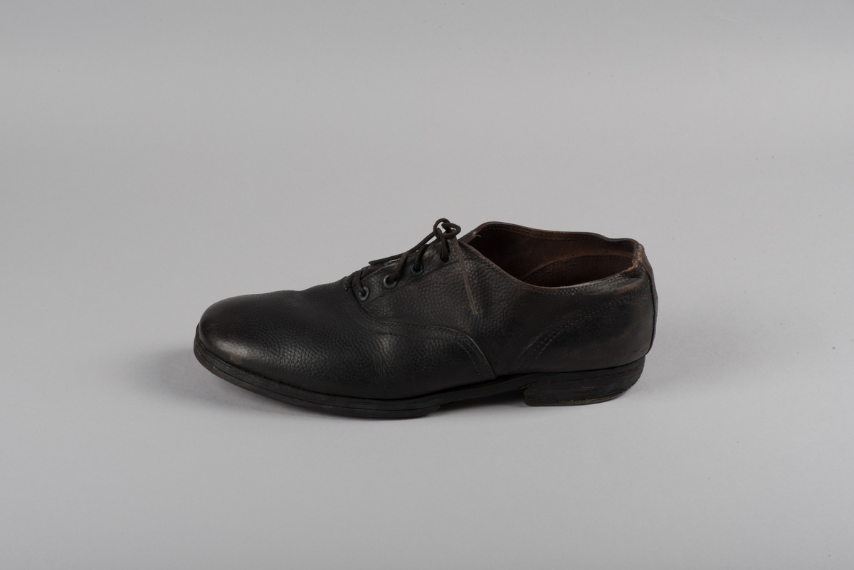 Herrsko, ett par, av skinn (läder) med sula av läder. Klacken skodd med metallsko i U-form. fyra par hål med öljetter i metall och lädersnöre. Ofodrade. Möjligen storlek 46 eller 40. Skinnet är präglat med ett möster av små stjärnor. 

På den högra skon är metallskoningen på klacken vänd, troligen omspikad. 

Skorna hör till en uppsättning kläder för en manlig fånge. 
Kläderna består av en kort dubbelknäppt rock, ett par byxor, en väst av grå vadmal, en mössa och en skjorta av oblekt linne.