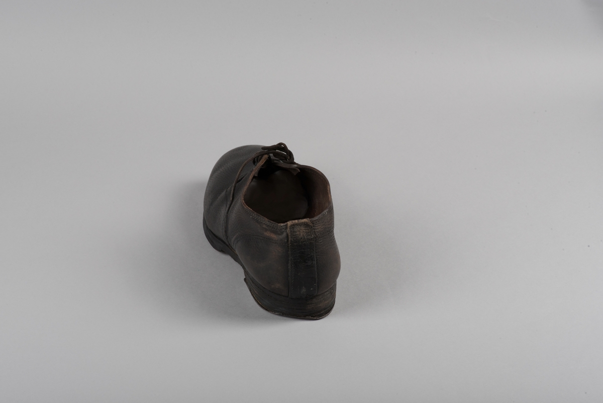 Herrsko, ett par, av skinn (läder) med sula av läder. Klacken skodd med metallsko i U-form. fyra par hål med öljetter i metall och lädersnöre. Ofodrade. Möjligen storlek 46 eller 40. Skinnet är präglat med ett möster av små stjärnor. 

På den högra skon är metallskoningen på klacken vänd, troligen omspikad. 

Skorna hör till en uppsättning kläder för en manlig fånge. 
Kläderna består av en kort dubbelknäppt rock, ett par byxor, en väst av grå vadmal, en mössa och en skjorta av oblekt linne.