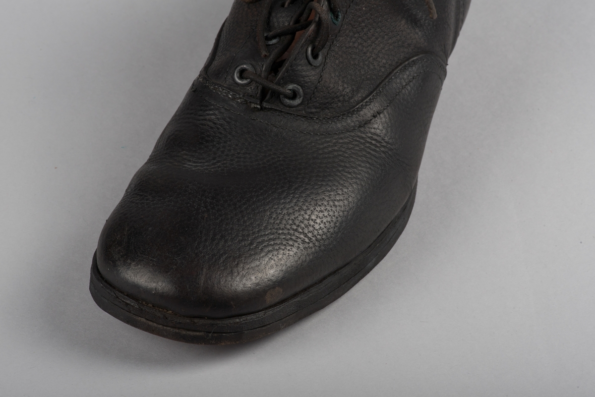 Herrsko, ett par, av skinn (läder) med sula av läder. Klacken skodd med metallsko i U-form. fyra par hål med öljetter i metall och lädersnöre. Ofodrade. Möjligen storlek 46 eller 40. Skinnet är präglat med ett möster av små stjärnor. 

På den högra skon är metallskoningen på klacken vänd, troligen omspikad. 

Skorna hör till en uppsättning kläder för en manlig fånge. 
Kläderna består av en kort dubbelknäppt rock, ett par byxor, en väst av grå vadmal, en mössa och en skjorta av oblekt linne.