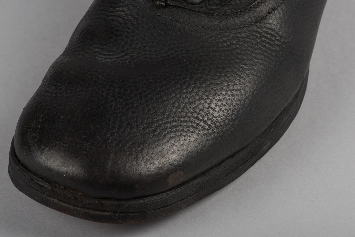 Herrsko, ett par, av skinn (läder) med sula av läder. Klacken skodd med metallsko i U-form. fyra par hål med öljetter i metall och lädersnöre. Ofodrade. Möjligen storlek 46 eller 40. Skinnet är präglat med ett möster av små stjärnor. 

På den högra skon är metallskoningen på klacken vänd, troligen omspikad. 

Skorna hör till en uppsättning kläder för en manlig fånge. 
Kläderna består av en kort dubbelknäppt rock, ett par byxor, en väst av grå vadmal, en mössa och en skjorta av oblekt linne.