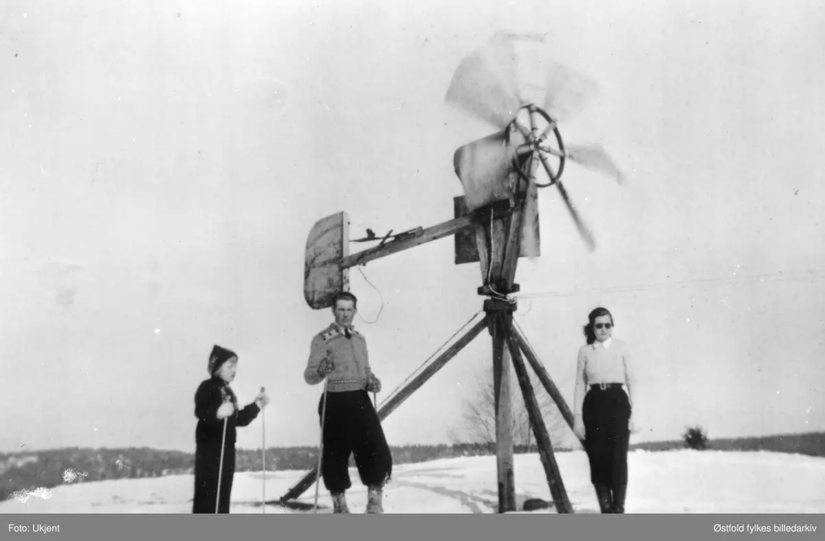 Vindmølle på gården Hauger i Varteig, ca. 1940-45. Vindmølla ble brukt under 2.verdenskrig til å produsere strøm. 
Fra venstre: Ingrid Sunnås, Rangar Sunnås, Astrid Bø-Hauger.
