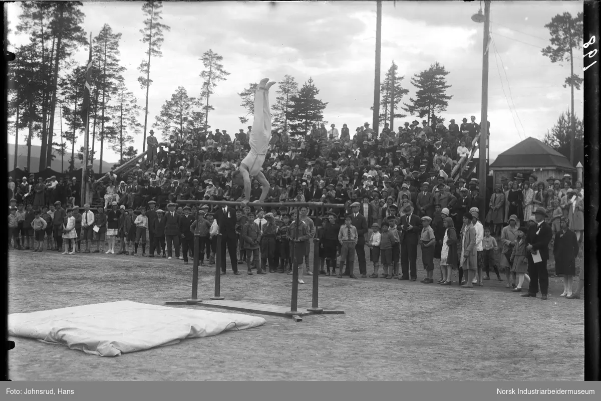 Kretsturnstevne 1930. Mann i øvelse skranke. Publikum står rundt idrettsanlegget.