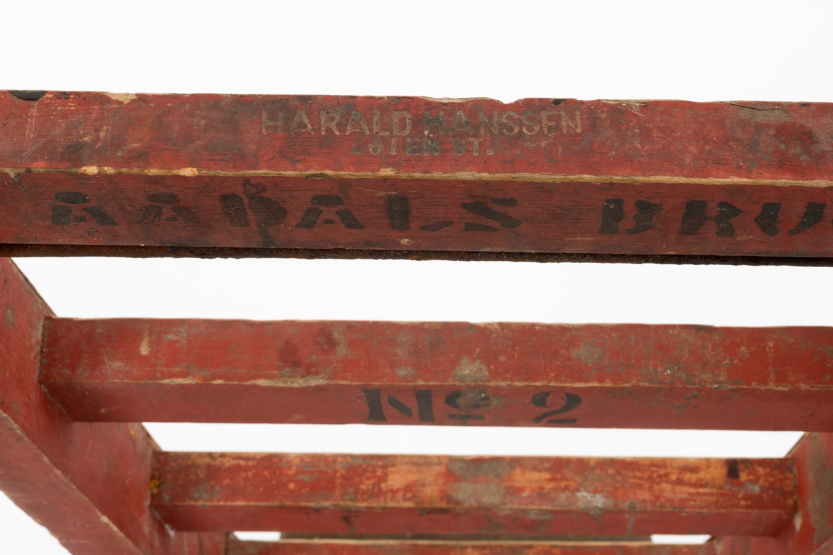 Sekketralle, lagd ved Aadals Brug Jernstøberi og Mekaniske Værksted, en bedrift som ble etablert ved Svartelva i Løten omkring 1840 og var i virksomhet til den ble herjet av brann i 1928. Sekketralla er lagd av jern og tre. Den er bygd på en 57 centimeter lang jernaksling, der den midtre delen har et rektangulært tverrsnitt (2.5 X 3,0 centimeter. I ytterendene av denne akslingen er det om lag 8 centimeter lange sylindriske endeledd med cirka 2,4 centimeters endetapper. På disse er det montert støperjernshjul med drøyt 22 centimeters diameter og 4,8 centimeter bred bane. Den nevnte banen er noe avskallet i ytterkant, særlig på det som sett i brukerens perspektiv er det venstre hjulet. Hjulene har fire grove eiker hver. På den nevnte akslingen er det montert ei treramme med to cirka 134 centimeter lange armer og fire tverrtrær som er inntappet mellom disse armene med en innbyrdes avstand på 13 centimeter. Tappingene er låst ved hjelp av et rundjern med gjengete ender som er tappet gjennom armene tett inntil det øverste tverrtreet og strammen ved hjelp av endemuttere med underliggende jernskiver. I fronten av tralla er det montert et skråstilt 35-36 centimeter bredt jernbrett i forlengelsen av beslagsstenger som beskytter trallearmenes oversider. Også de fremre endene av armenes undersider, der det også er klosser som akslingene er forankret i, er jernbeslåtte. Avstanden mellom trallearmene tiltar noe fra den fremre mot den bakre enden. Her er de gitt et avrundet tverrsnitt, slik at de skulle kjenes gode å holde i. På undersida, like framfor handtakene, er det inntappet 9 centimeter høye treføtter, fastlåst ved hjelp av gjennomgående jernbolter fra jernbeslagene på oversida av armene. Tralla er malt med en rødbrun farge. På undersidene av de to øverste tverrtrærne finner vi tekstene «AADALS BRUG» og «No 2», påført med svart maling ved hjelp av sjablong. På det øverste tverrtreet finner vi også svijernstempelet «HARALD HANSSEN  LØTEN ST.». Harald Hanssen drev kolonialbutikk i Brenneriroa i Løten.