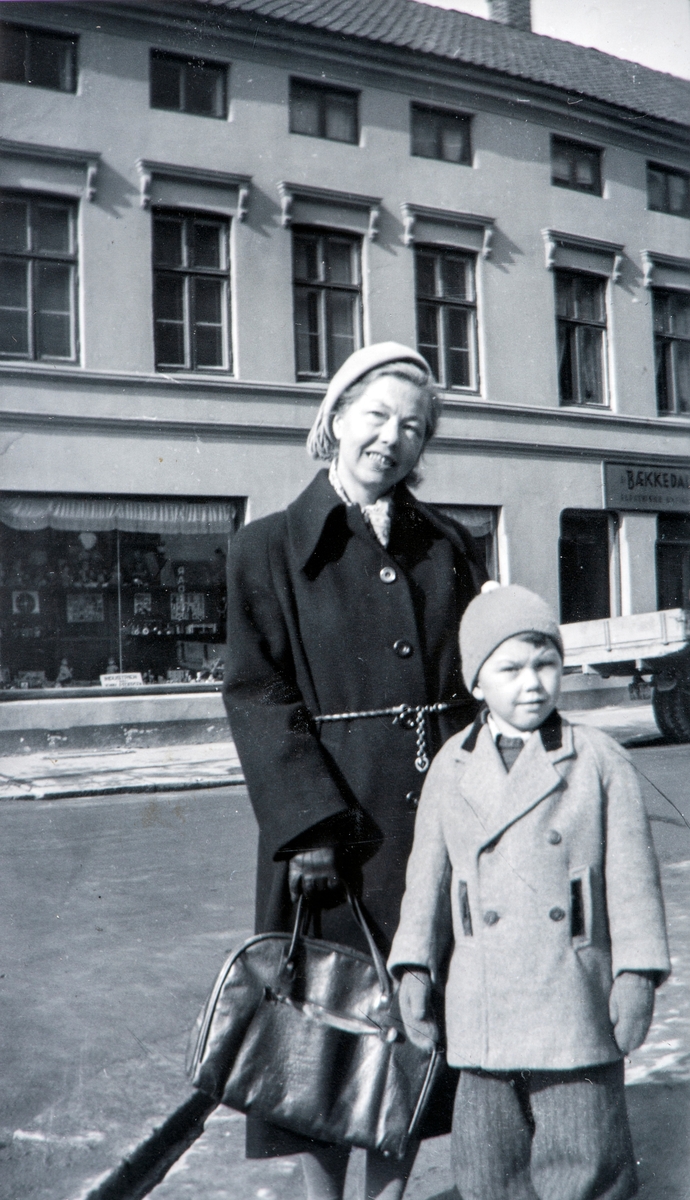 Mor Vegerd Hesselberg og sønn Arne på handletur i Hamar. Tatt fra Norrøna-hjørnet, Torggata 15 over Enggata mot Svenkerud-gården Torggata 21, rundt 1953.