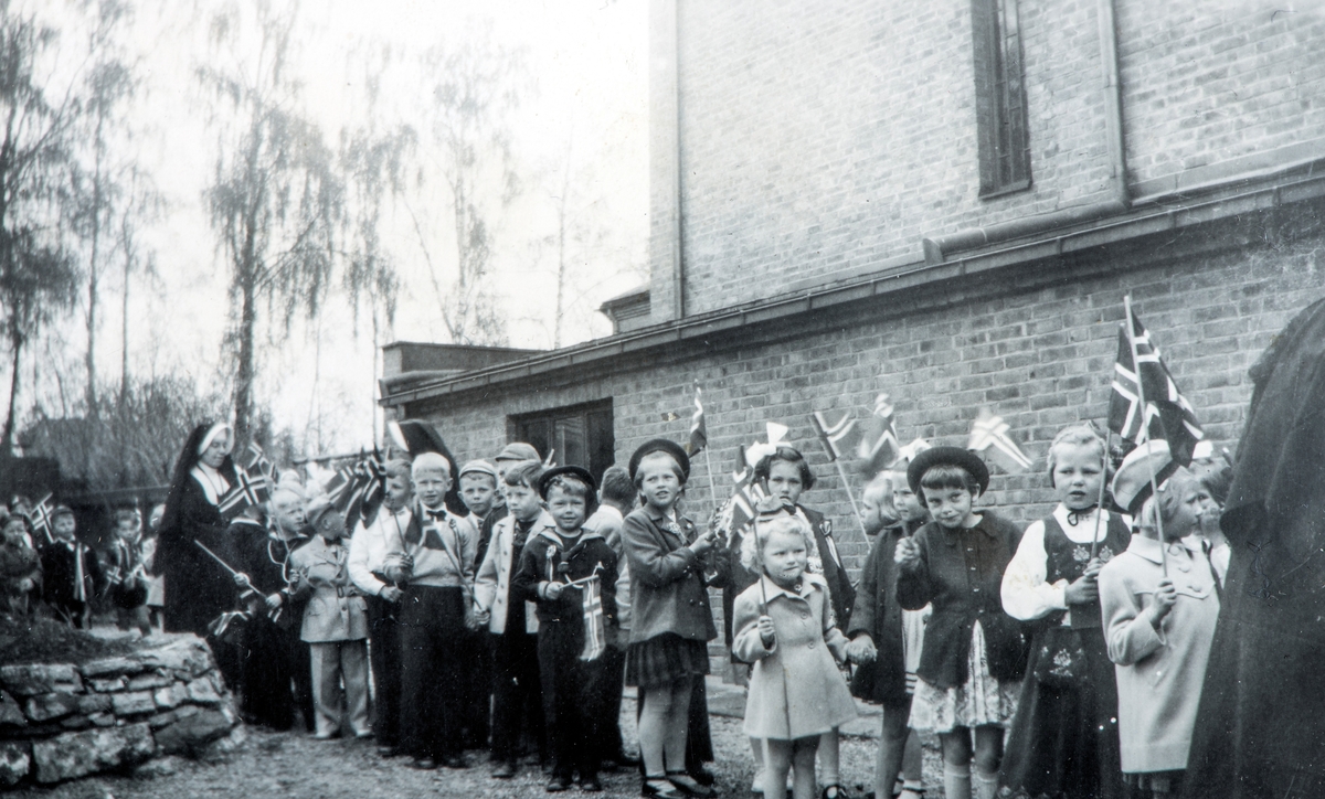 17. mai tog. Tatt 17. mai rundt 1953 inne i gårdsrommet til Torggata 113, mot den vestre veggen til St. Torfinn kirke. Før "Skoletoget" starter. Antagelig søster Sunniva i bakgrunnen.