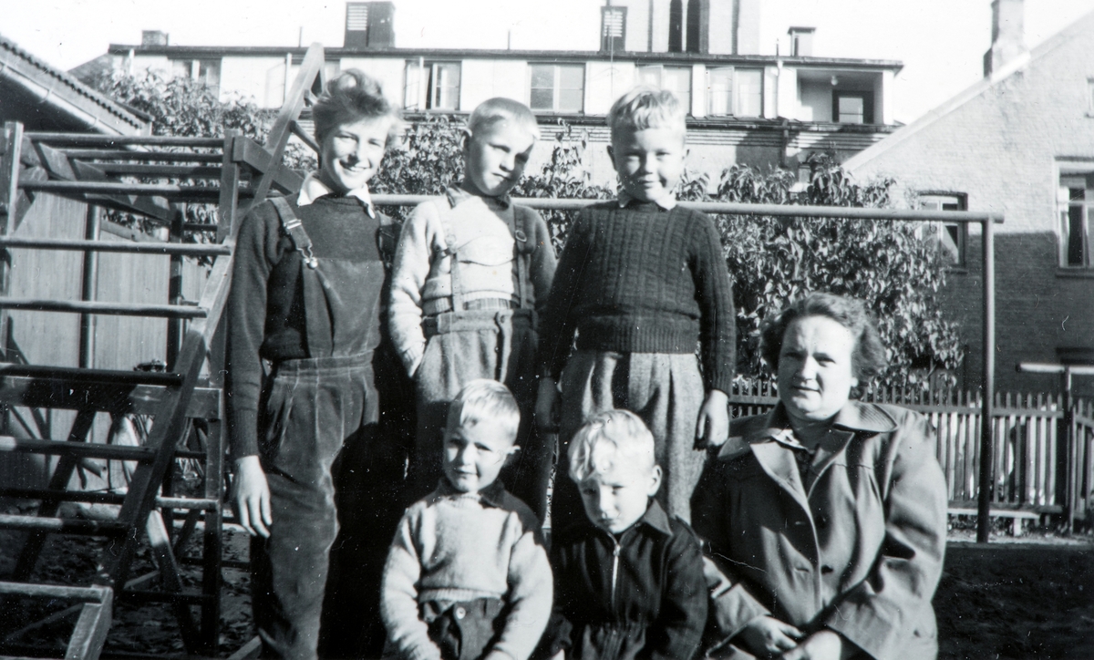 Gruppe bilde tatt inne på  St. Torfinn barnehage, i gårdsrommet til Torggata 113 mot den vestre veggen til St. Torfinn klinikk og Getz-villaen t.h., Lekeapparater til St. Torfinn barnehage, klatrestativ t.v. og husker bak. Fire gutter,  Arne Hesselberg bakerst til høyre - og to barnehage"tanter".