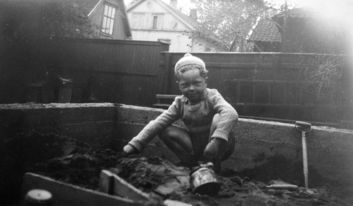 Barn i sand-kasse. Arne Hesselberg leker i sandkassa. St. Torfinns Barnehage. 
Tatt mot vest. Nåværende prestegård Høyesalgata 21 - Rud-villaen - bakut venstre, på den andre siden av gata Høyensalgata 22.