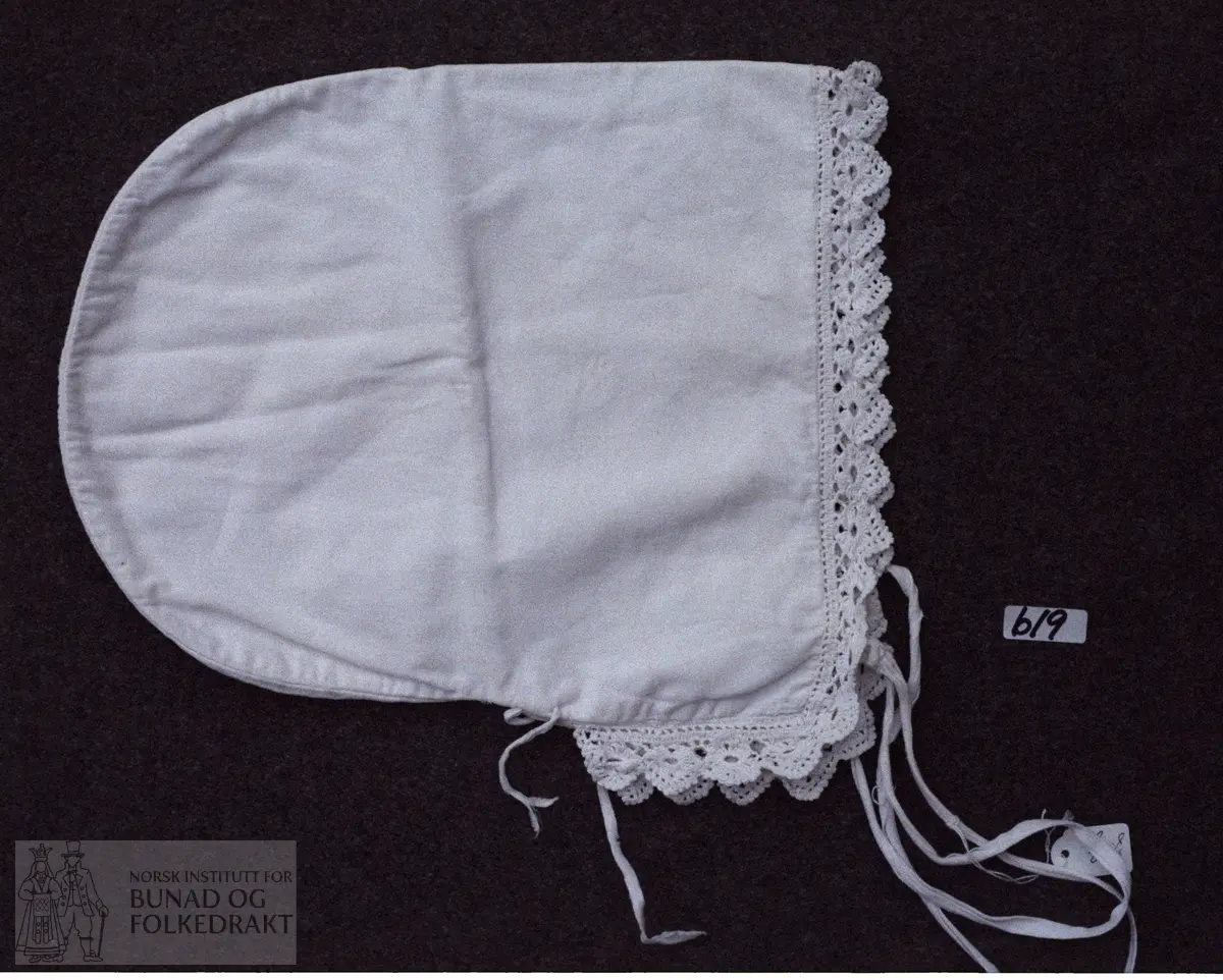 Foto av Henrikka Hallvardtr. Wergeland, f. 1868, og mannen.  Kvitehue.  -  Matr.:  Kvitt bomullslerret med hekla blonde. Knyteband av kvitt bendelband. Trekksnor av smalt bendelband.