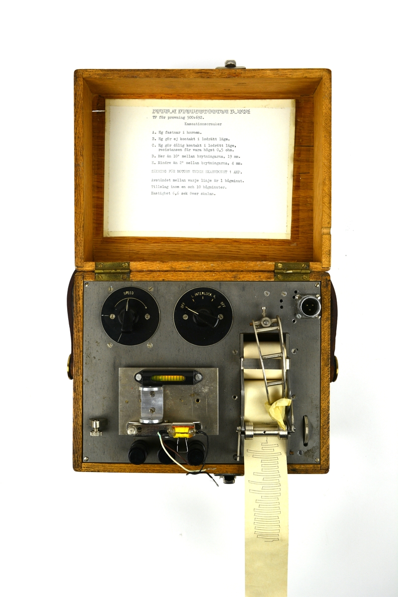 Provapparat kvicksilverströmbrytare. Provutrustning i metall monterad i brun trälåda. Innehåller instruktioner i insidan av locket samt medföljande lös manual med skötselinstruktioner.