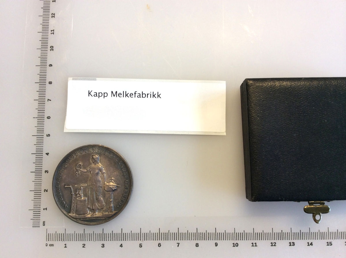 Etui med gråfarget mynt avbildet med en karakter fra gresk eller romersk mytologi på den ene siden og en laurbærkrans på den andre