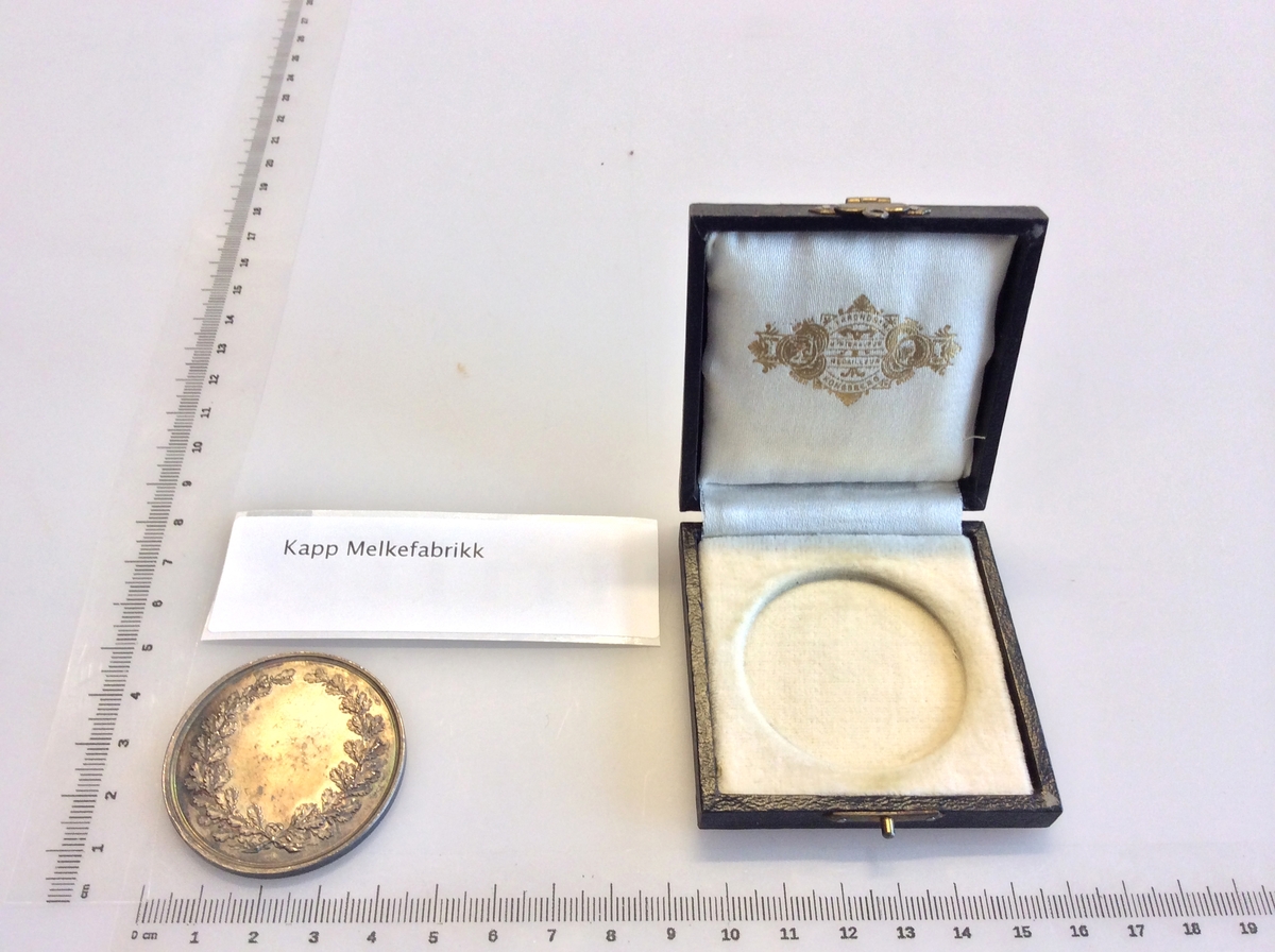 Etui med gråfarget mynt avbildet med en karakter fra gresk eller romersk mytologi på den ene siden og en laurbærkrans på den andre