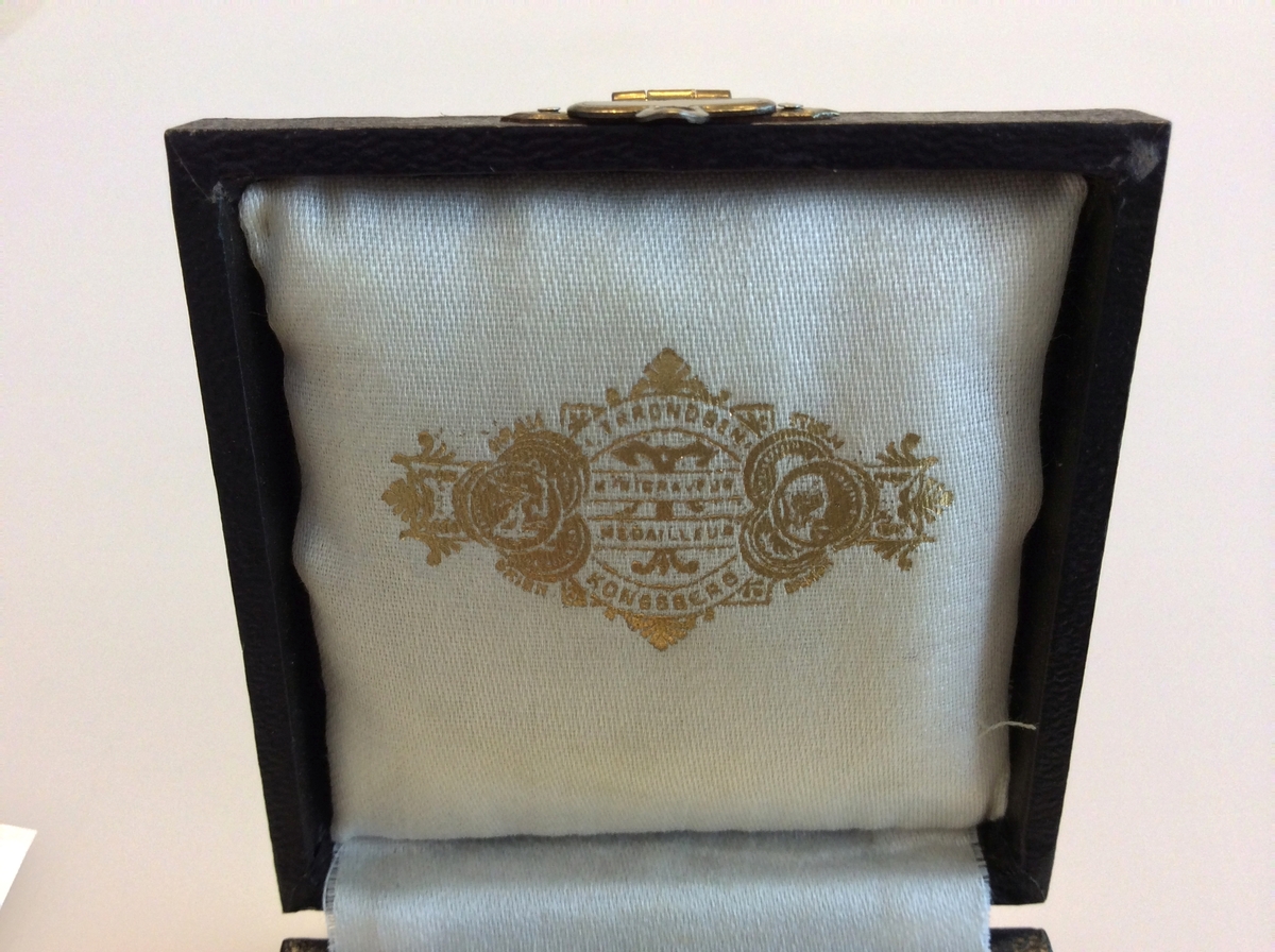 Etui med gråfarget mynt avbildet med en karakter fra gresk eller romersk mytologi på den ene siden og en laurbærkrans på den andre