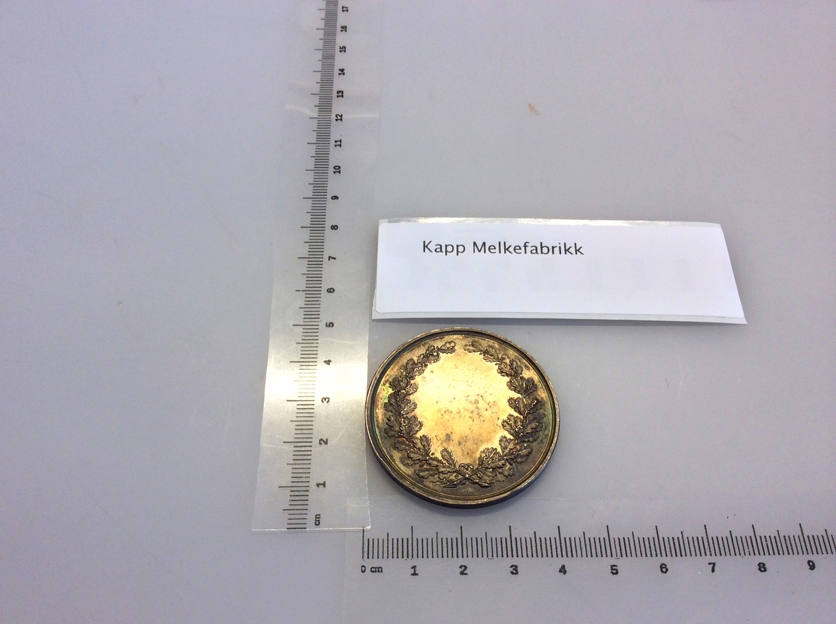 Etui med gråfarget mynt avbildet med en karakter fra gresk eller romersk mytologi på den ene siden og en laurbærkrans på den andre