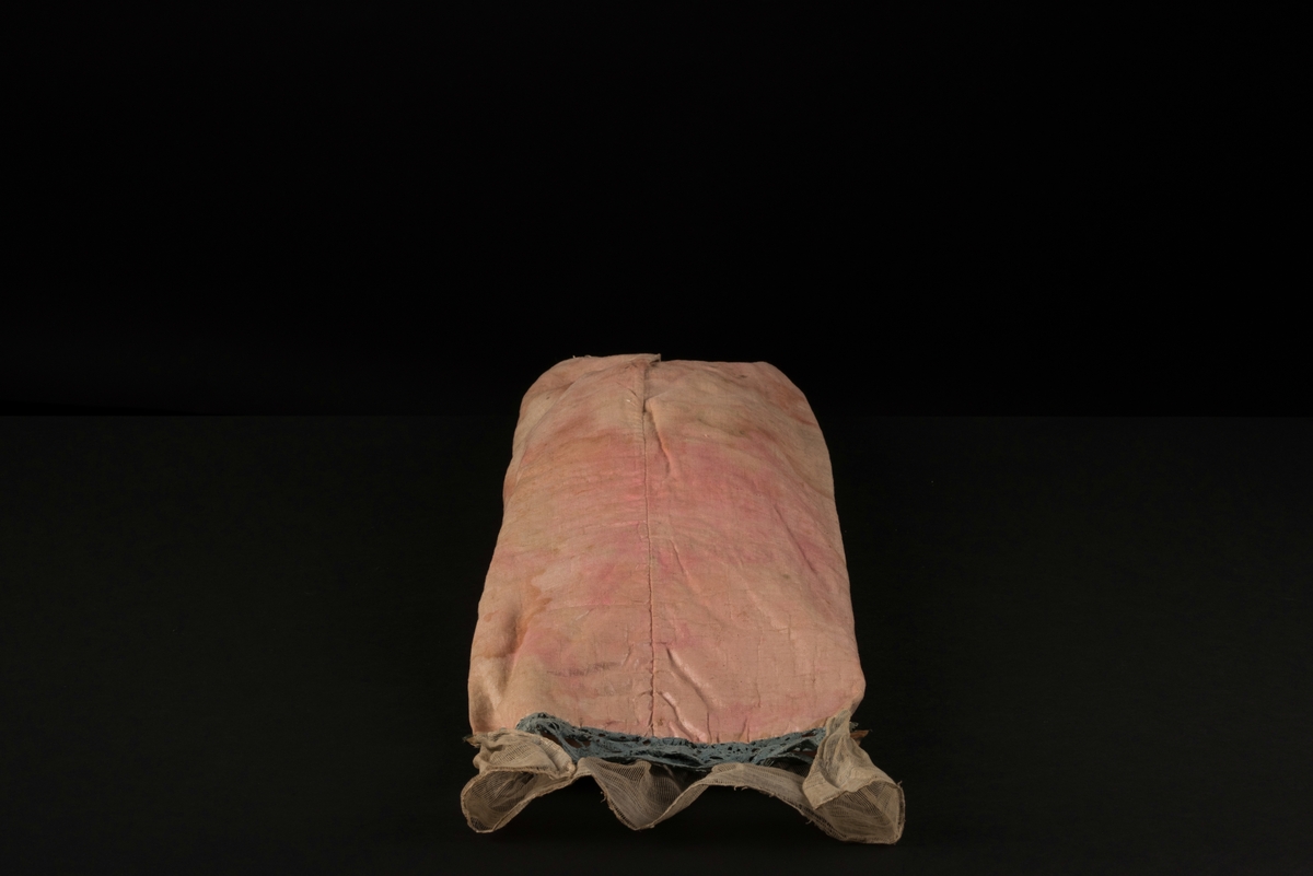 Doppåse till nyfödd. Utsidan sydd av rosarött linnetyg, mycket blekt. Påsen avsmalnande upptill med lagda veck och sprund i ryggen. Har troligtvis burits med en krage eller krås. 

Påsens nedre del avslutas med en blå spets under tyll i vitt med blå inslag. 

Påsen är dekorerad med sidenband och bomullsband som bildar kryss samt en blå rosett. 

På påsens mittfält sitter två runda dekorationer den ena 150 mm i diameter och den andra 120 mm i diameter. Den större dekorationen har 5 speglar och metalltrådar som bildar blommor. Runt hela sitter en blå spets. Den mindre dekorationen har en större spegel, denband och blommor i metalltråd.