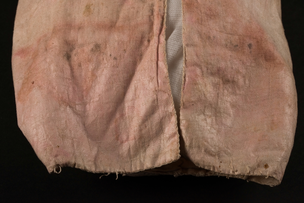 Doppåse till nyfödd. Utsidan sydd av rosarött linnetyg, mycket blekt. Påsen avsmalnande upptill med lagda veck och sprund i ryggen. Har troligtvis burits med en krage eller krås. 

Påsens nedre del avslutas med en blå spets under tyll i vitt med blå inslag. 

Påsen är dekorerad med sidenband och bomullsband som bildar kryss samt en blå rosett. 

På påsens mittfält sitter två runda dekorationer den ena 150 mm i diameter och den andra 120 mm i diameter. Den större dekorationen har 5 speglar och metalltrådar som bildar blommor. Runt hela sitter en blå spets. Den mindre dekorationen har en större spegel, denband och blommor i metalltråd.