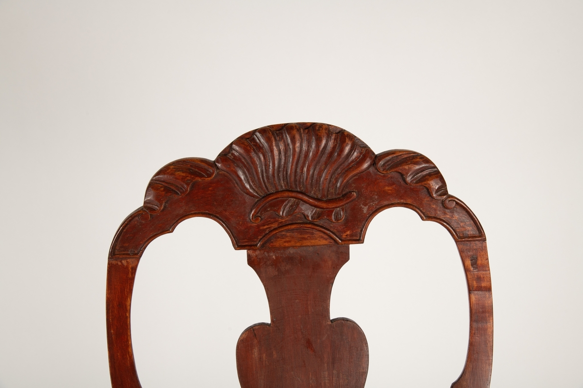 Høy, åpen, svungen rygg med balusterformet midtbrett,  toppstykke utskåret med skjell og blad. Løst sete  nedfelt i sargen, stoppet med sjøgress, trukket med blomstret trekk (ca. 1910). Svungne armlener.  Tunget sarg med skjell og blad utskåret i fronten,  svungne ben med skjell-løv på kneet, spiss fot.  Ingen bindeledd mellom benene.