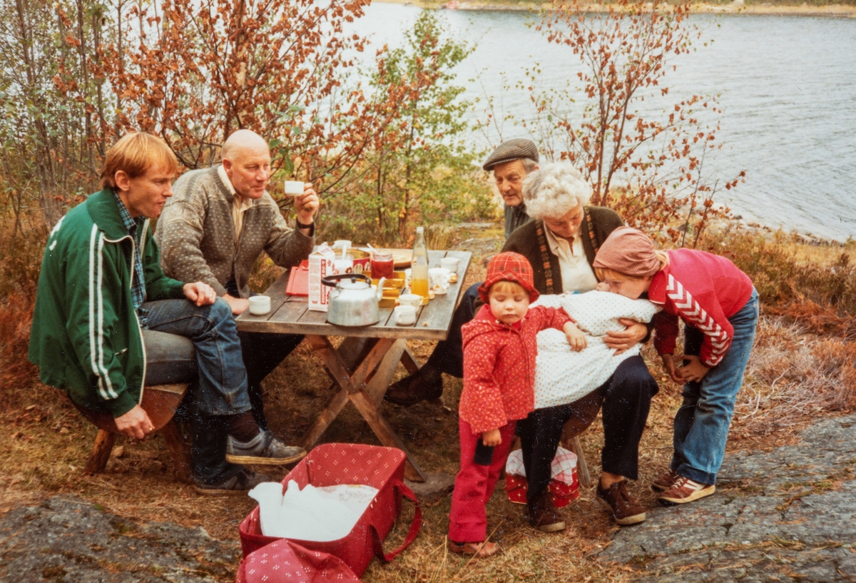 Høgsdagskaffe, kaffepause, kafferast på Tronsbakkhytta ved Harasjøen 1982. Fra venstre: Øystein Mæhlum, Arne Frydenlund, Per Mæhlum, Ingrid Mæhlum med Kersti Mæhlum på fanget, Gina Mæhum bøyd og fremst Mari Mæhlum.
