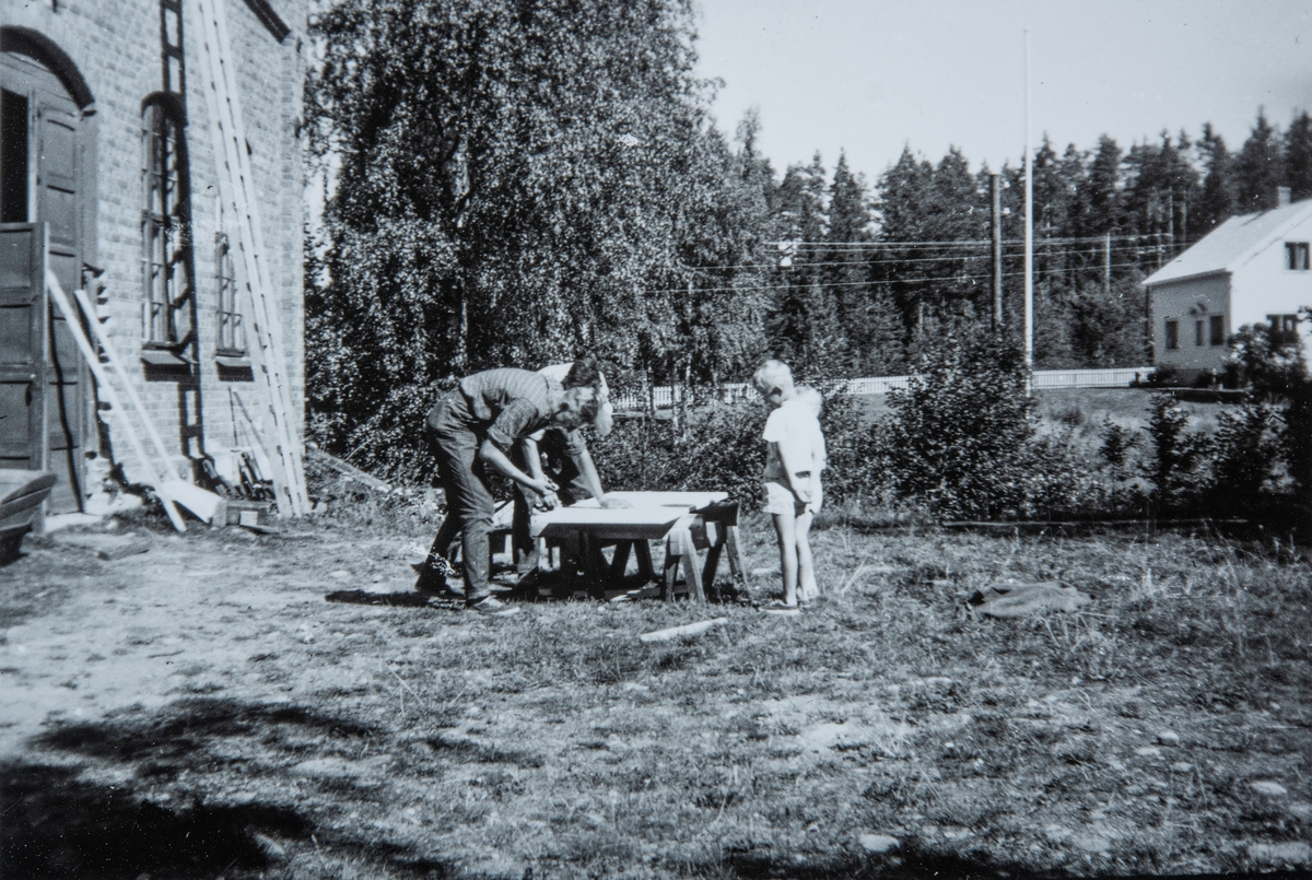 Produksjon av frysere og kjølesystemer i Vallset. Arne Frydenlund. 
To barn står å ser på, utenfor "stasjon" på Vallset. Utenfor den gamle kraftstasjonen Fosselva I i Vallset 1959. De to barna til høgre er Torkel og Eli Frydenlund.