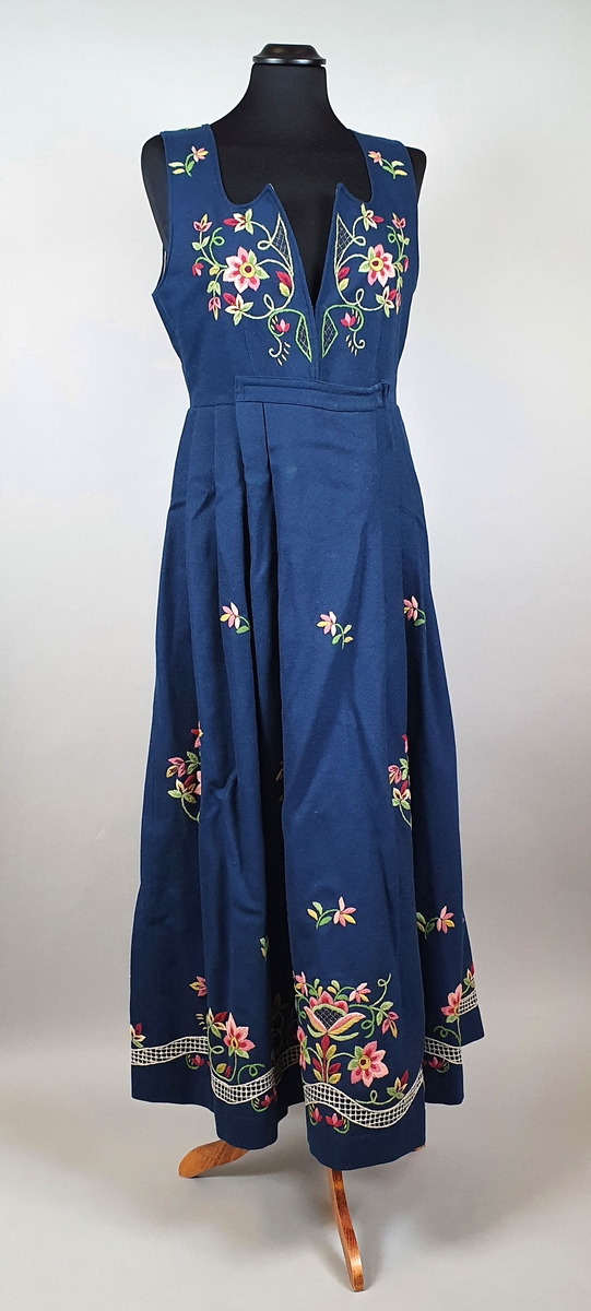Lundebybunad i tre deler; livkjole, løslomme og lue. Bunaden er mørkeblå med brodert stilisert blomstermotiv på stakken og på livet, både på ryggen og forstykkene.