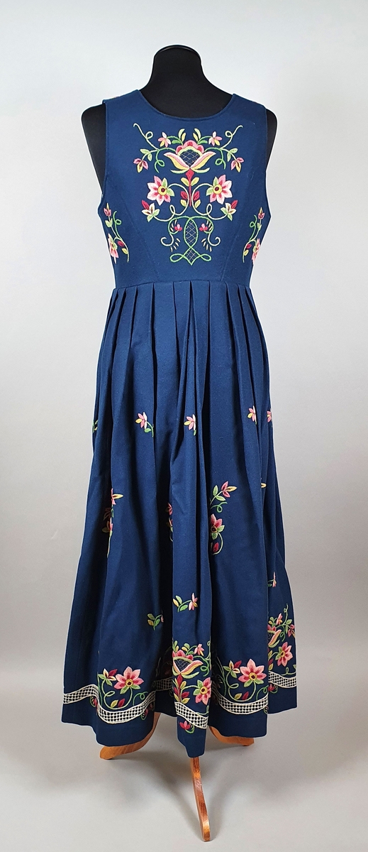 Lundebybunad i tre deler; livkjole, løslomme og lue. Bunaden er mørkeblå med brodert stilisert blomstermotiv på stakken og på livet, både på ryggen og forstykkene.