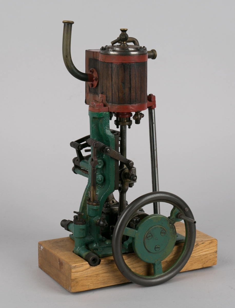 Dampmaskinmodell, 1- sylindret med oppstående kjele/dobbel plate av tre  og metall med dreiehjul på siden.  Montert på tresokkel.