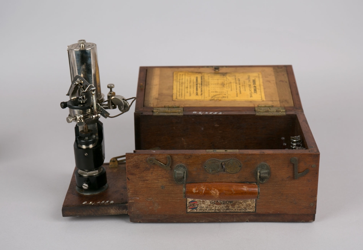 Maskinindikator.  Indikatoren er festet til ene kortsiden av trekasse og vippes ut ved bruk. Kassen har lokk med hengsler, innvendig hengslet plate til romavdeler og oppbevaringsfester for løse deler. 