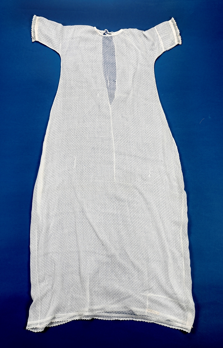 Dåpskjole med underkjole og belte.
Kjolen har rund hals med løpegang og knytesnor. Hele kjolen er klippet i ett stykke. skjøtt stoff på det ene ermet. Blondepynt i alle åpninger.  
Underkjolen er klippet i ett stykke. Rynket i halsen. Splitt bak med knepping øverst.
Bredt bånd der alle dåpsbarnas navn er brodert med henholdsvis blå og rosa skrift.