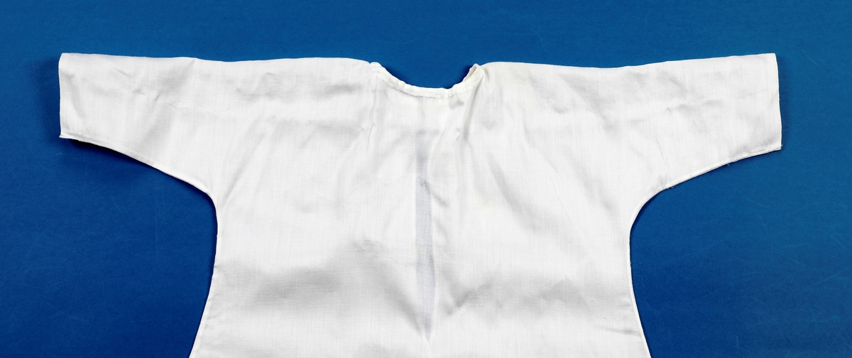 Dåpskjole med underkjole og belte.
Kjolen har rund hals med løpegang og knytesnor. Hele kjolen er klippet i ett stykke. skjøtt stoff på det ene ermet. Blondepynt i alle åpninger.  
Underkjolen er klippet i ett stykke. Rynket i halsen. Splitt bak med knepping øverst.
Bredt bånd der alle dåpsbarnas navn er brodert med henholdsvis blå og rosa skrift.