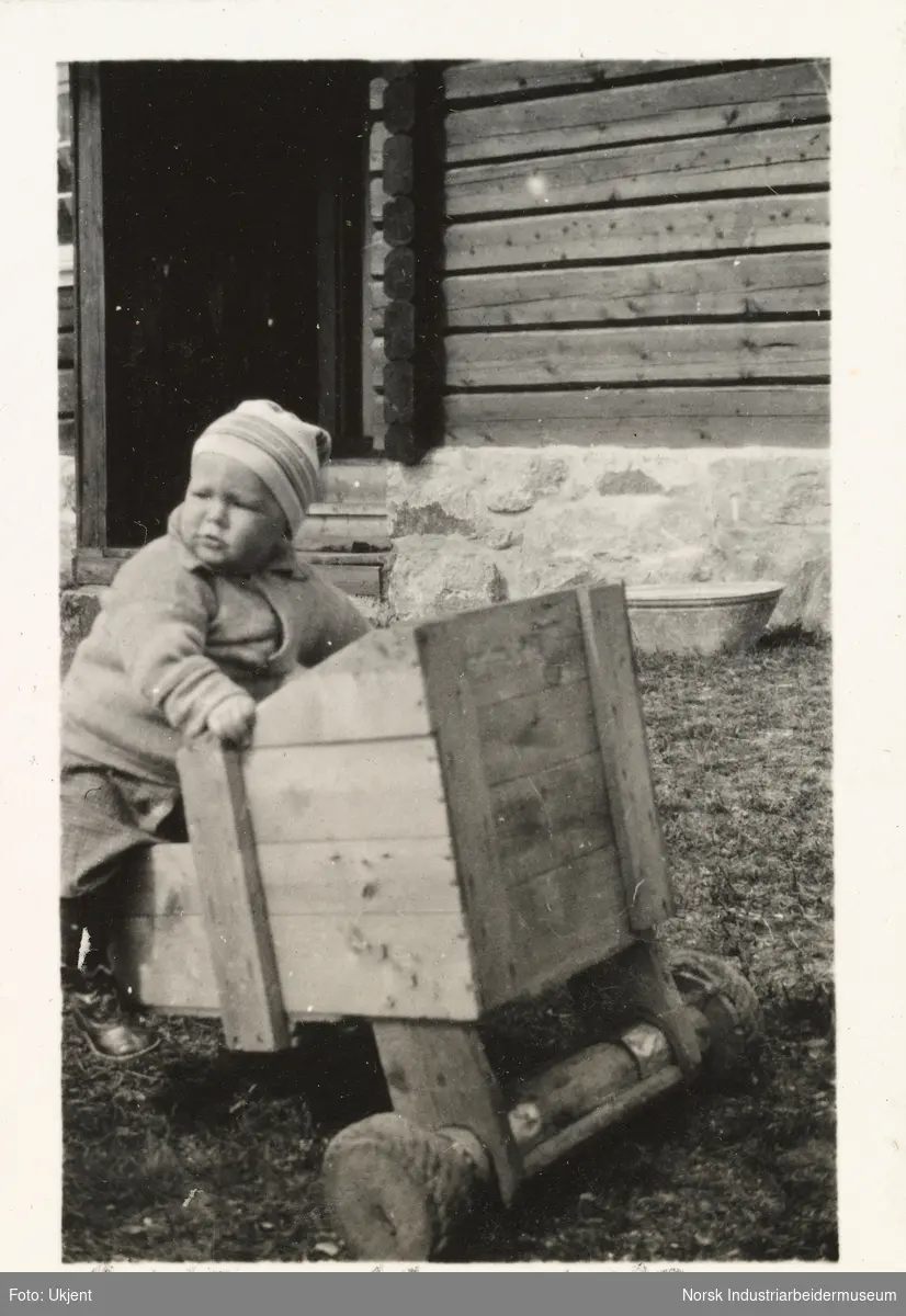 Briskeroe på Møsstrond. Liten gutt, Sven Hartvig, sitter i en trekasse med hjul på tunet.