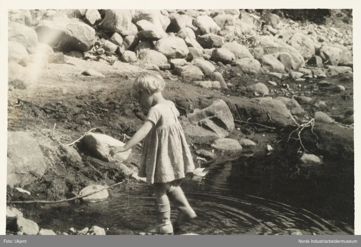 Møsstrond 1928.  Et barn i kjole leker i en vannpytt