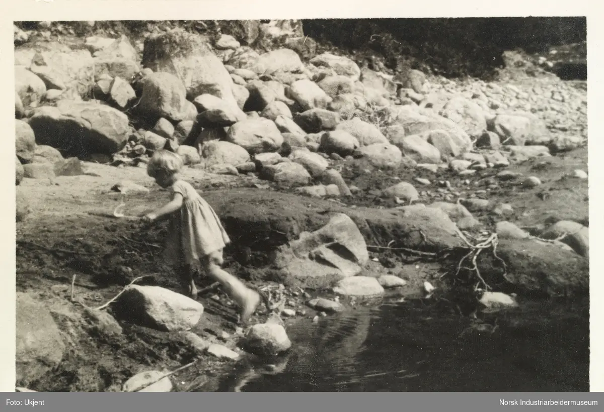 Møsstrond 1928.  Et barn i kjole leker i en vannpytt