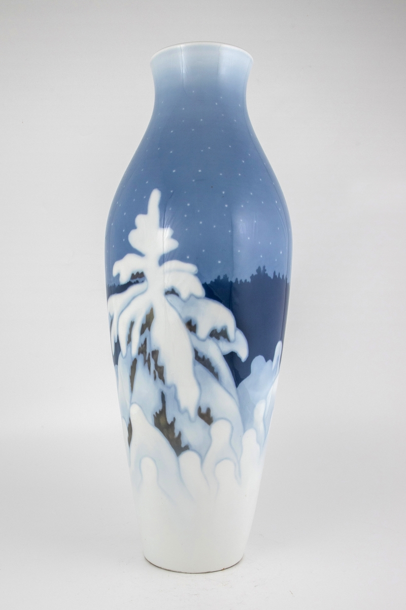 Forgrunnen domineres av et grantre dekket av snø, samt en rekke av mindre trær. I mellomgrunnen skimtes konturene av en mørkeblå ås, mens en blekblå nattehimmel med stjerner utgjør bakgrunnen.