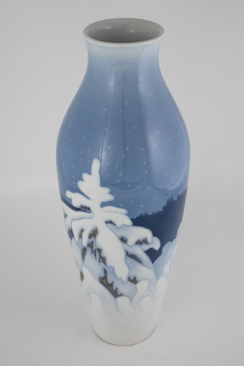 Forgrunnen domineres av et grantre dekket av snø, samt en rekke av mindre trær. I mellomgrunnen skimtes konturene av en mørkeblå ås, mens en blekblå nattehimmel med stjerner utgjør bakgrunnen.